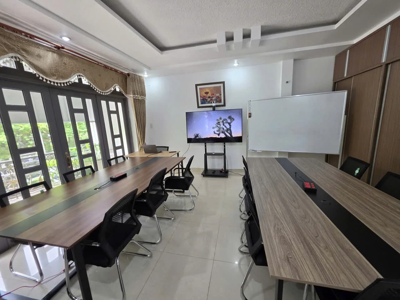 Phòng học với hai dãy bàn, cửa sổ bên trái, màn hình và bảng ở phía trước